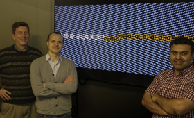 Three scientists in front of a crystalline material simulation image