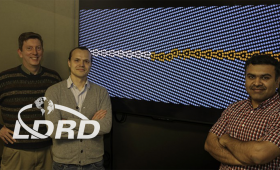 Three scientists in front of a crystalline material simulation image