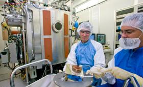 Two researchers load a mask blank into equipment for smoothing