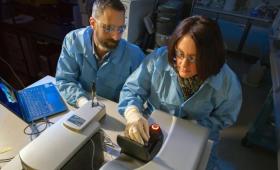 Two scientists sit at table with lab machinery