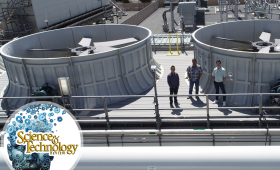 Three people standing on top of building with large fan units