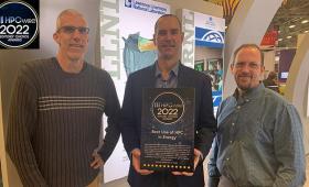 Three people facing camera, center person holds award plaque