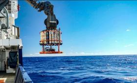 Ocean, with horizon, ship at left, and scientific equipment with gas tanks suspended from crane on ship