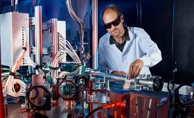 Man working behind lab bench with metal boxesm tubes, wires.