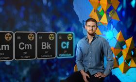 Wide shot of Gauthier sitting in front of a periodic table